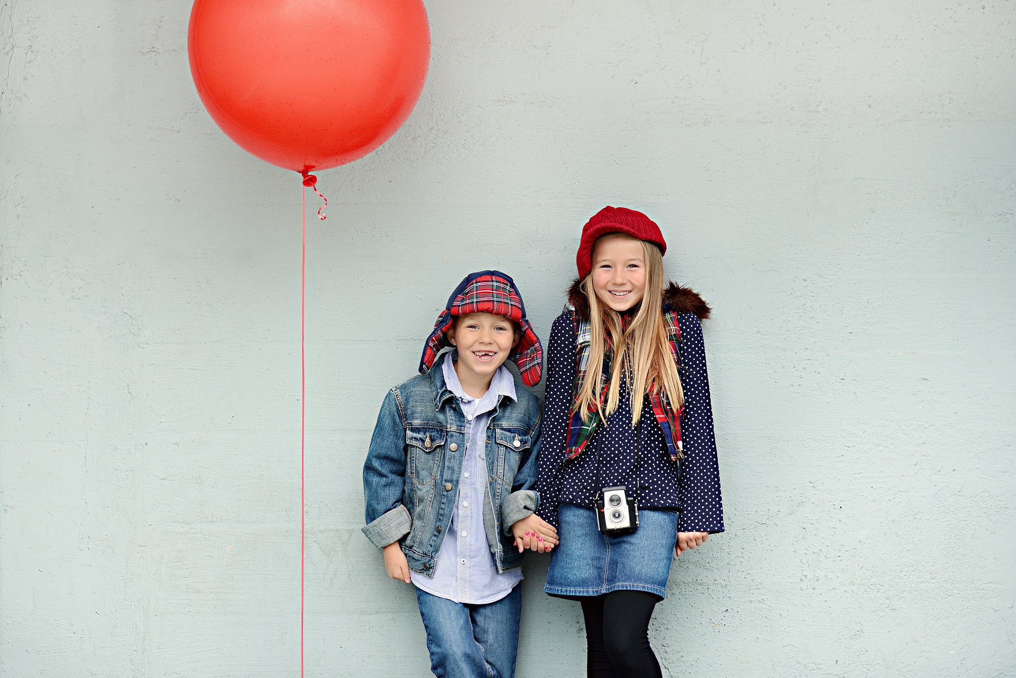 BOY AND GIRL STANDING IN FRONT OF BLUE WALL WITH RED BALLOON