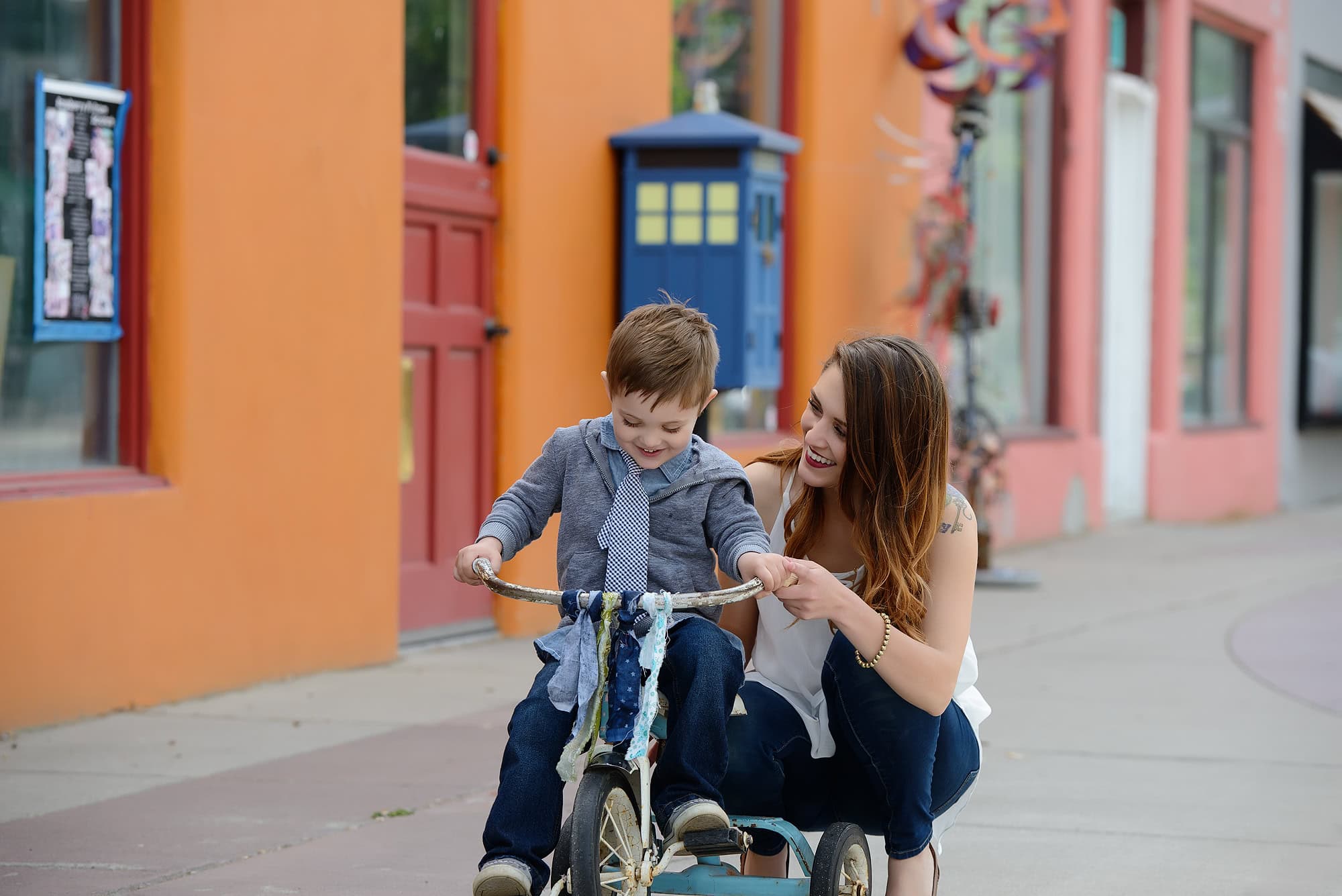 MOM LOOKING AT SON ON A TRICYCLE IN FRONT OF ORANGE WALL