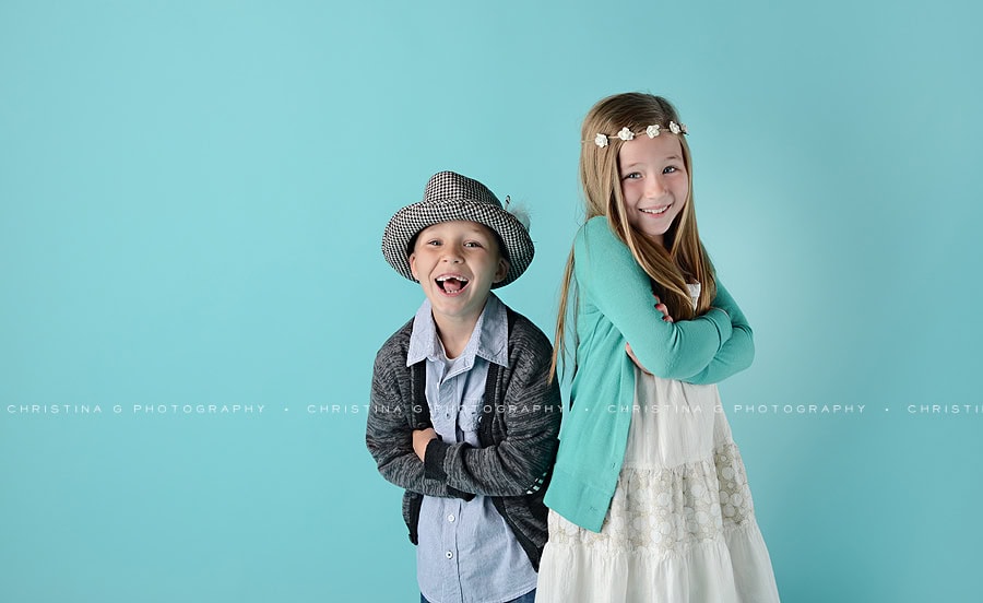 BOY AND GIRL IN STUDIO IN FRONT OF TURQUOISE BACKDROP SMILING