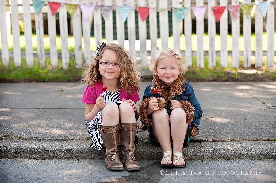 TWO LITTLE GIRLS SITTING ON SIDEWALK WITH LOLLIPOPS