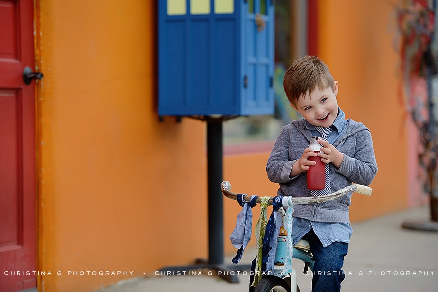 LITTLE BOY WITH A TIE IN FRONT OF COLORFUL WALL ON TRICYCLE